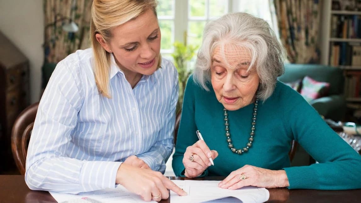 A caregiver helping an elderly woman review and sign a document at home